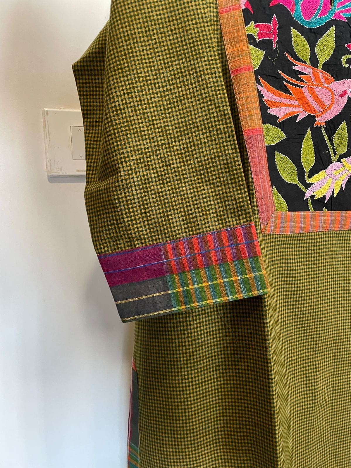 Close-up of the olive checked sleeve, its multicoloured checked cuff and the embroidered bird panel