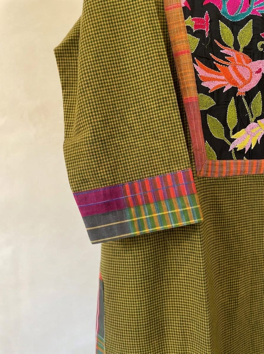 Close-up of an olive checked sleeve with a multicoloured checked cuff beside a panel of bird and flower embroidery