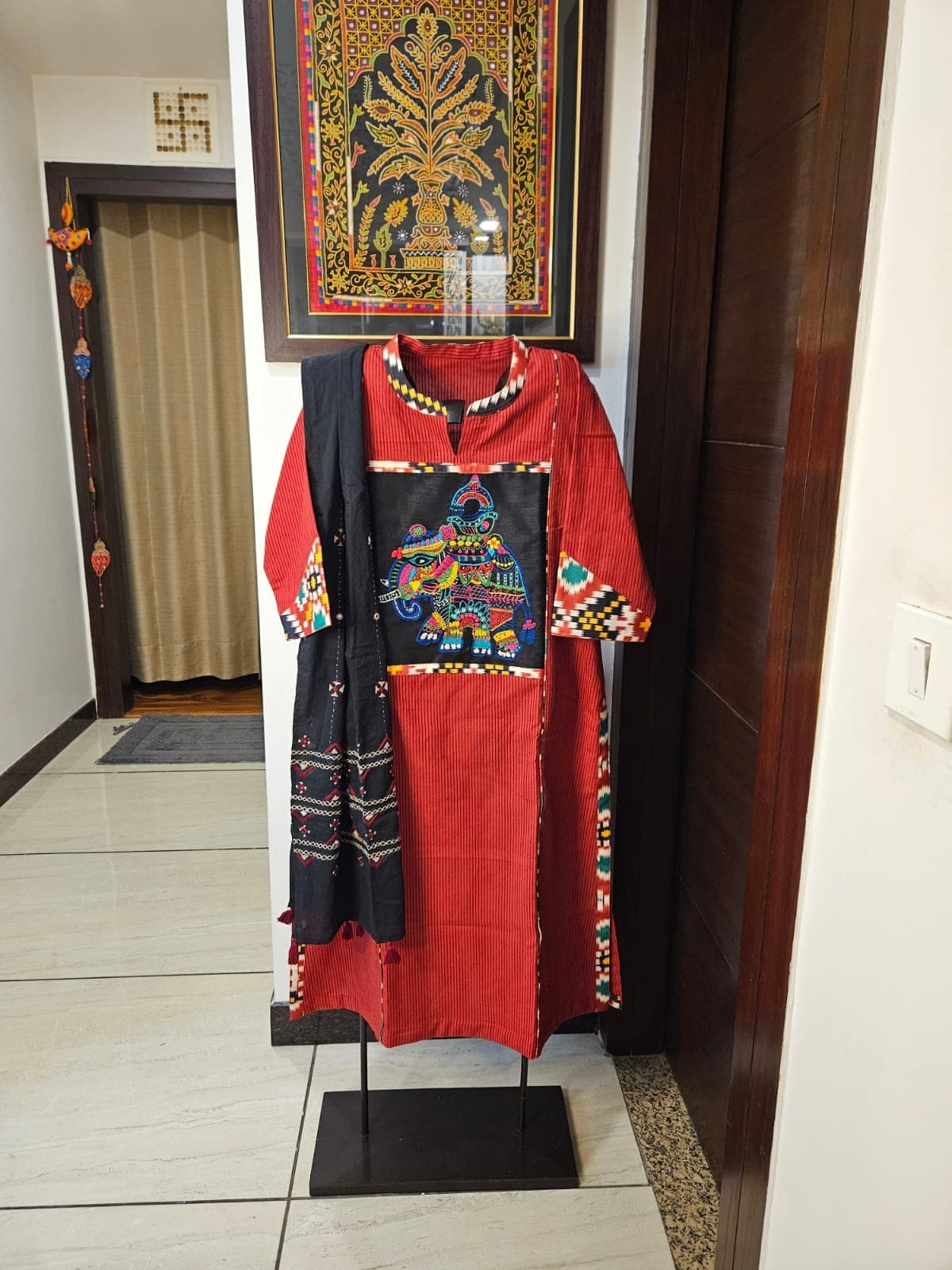 Red ikat kurti with a black embroidered elephant panel and patterned borders, with a black dupatta, on a stand in a hallway
