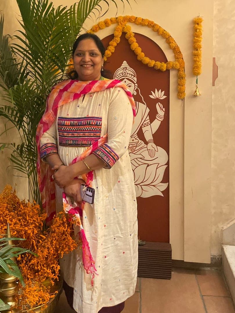 Hema Agarwal smiling at home, in an ivory kurti with an embroidered yoke and a pink and orange dupatta