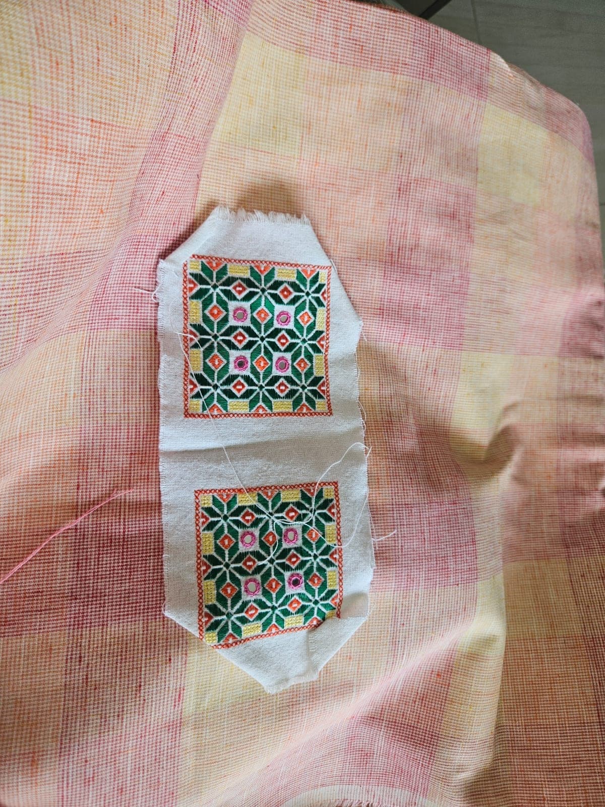 A geometric embroidered patch on checked fabric, its threads still loose